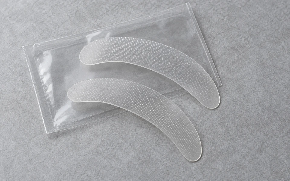 AI-generated illustrative product concept Curved brow-area cosmetic microneedle patch prototypes and a transparent sleeve
